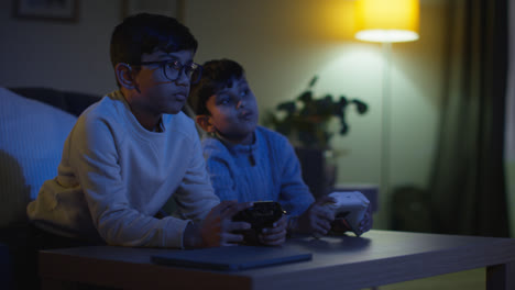 Two-Young-Boys-At-Home-Playing-With-Computer-Games-Console-On-TV-Holding-Controllers-Late-At-Night-7